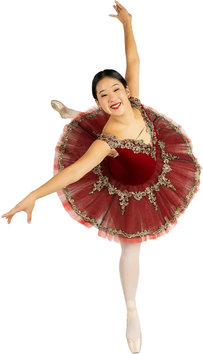 Ballerina in a burgundy and gold classical tutu posing on pointe with one arm overhead